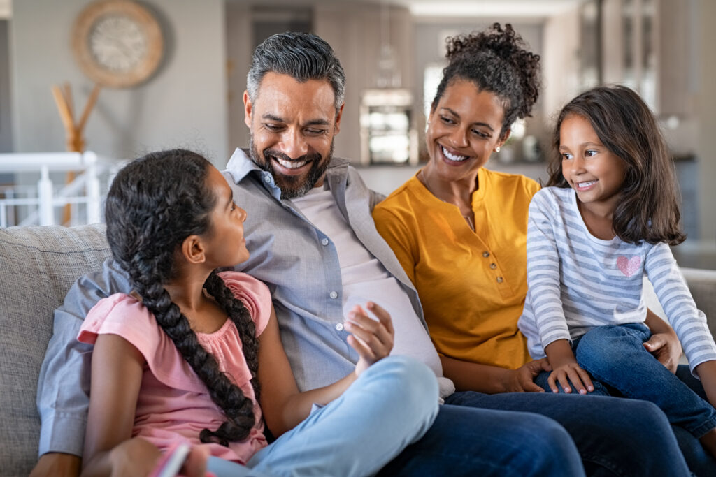 stock-photo-cheerful-multiethnic-family-at-home-sitting-on-sofa-listening-to-daughter-happy-couple-with-two-1889548987