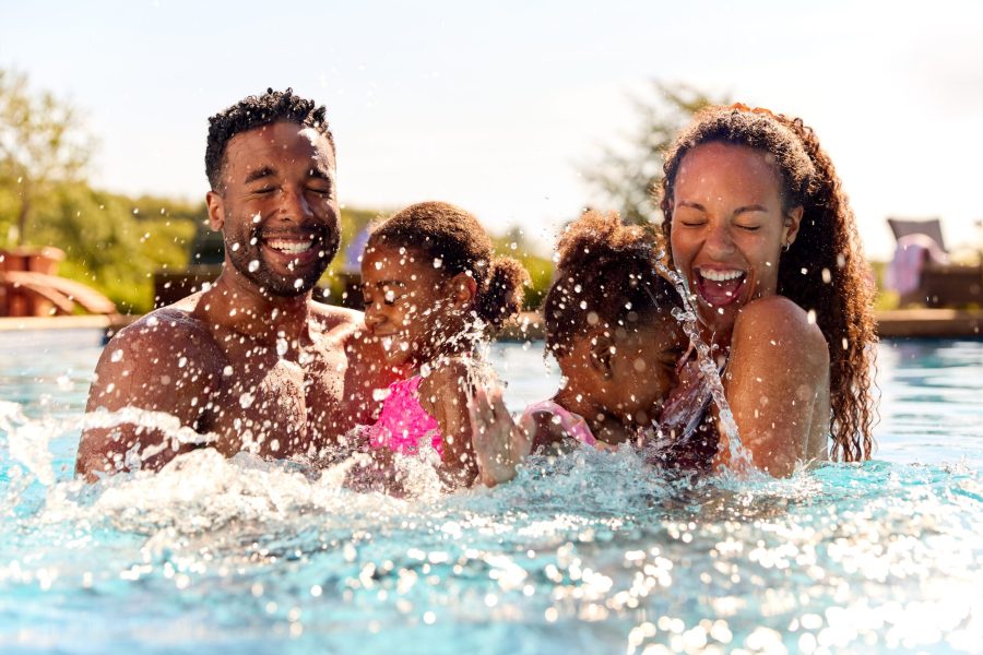 stock-photo-family-on-summer-holiday-with-two-girls-being-held-in-swimming-pool-by-parents-and-splashing-2198374313