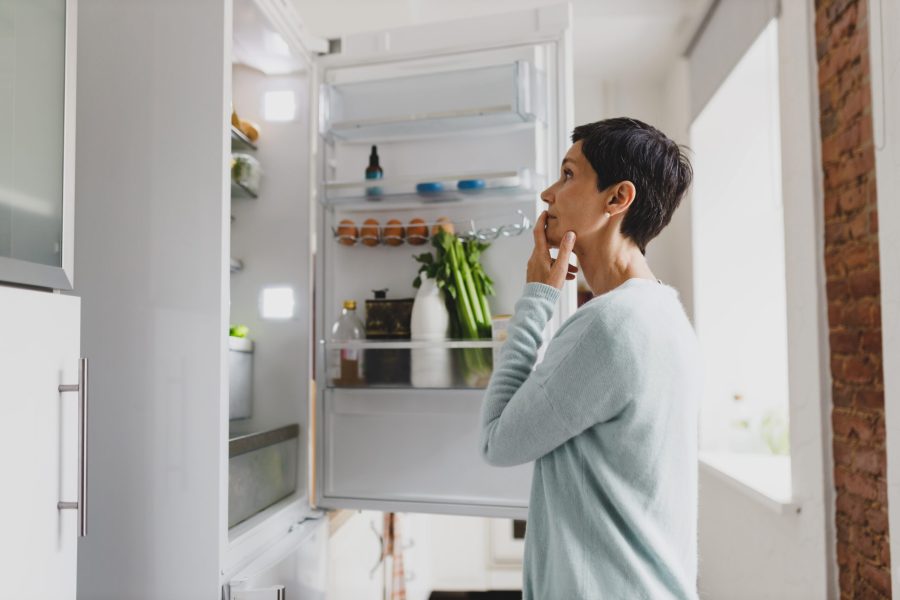 stock-photo-side-view-of-mature-female-with-short-hair-standing-in-front-of-opened-refrigerator-at-home-with-2486003153